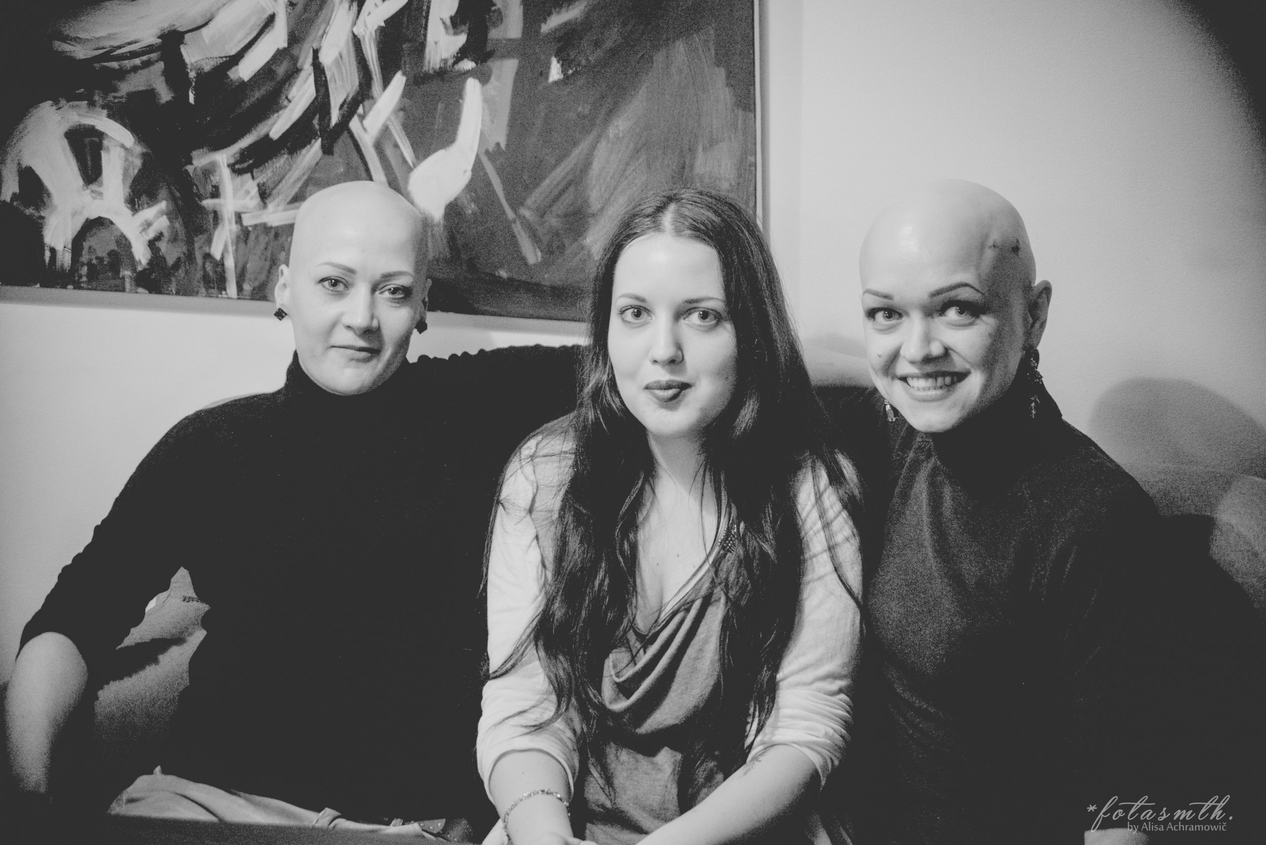 Изображение: Фото Alisa Achramowić / Черно-белая фотография трех женщин. На снимке – героини материала Ира и Катя вместе с авторкой текста. Они сидят на диване, на фоне светлой стены и картины с абстрактным сюжетом. Девушки улыбаются, глядя в камеру.